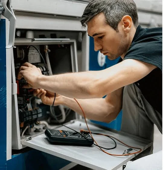 Technician testing electrical components inside HVAC equipment with a multimeter